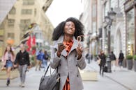 阳光明媚的一天，快乐的非洲妇女拿着智能手机和太阳镜走在街上