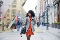 一位穿着灰色外套的时尚女性在充满活力的城市街道上散步时发短信