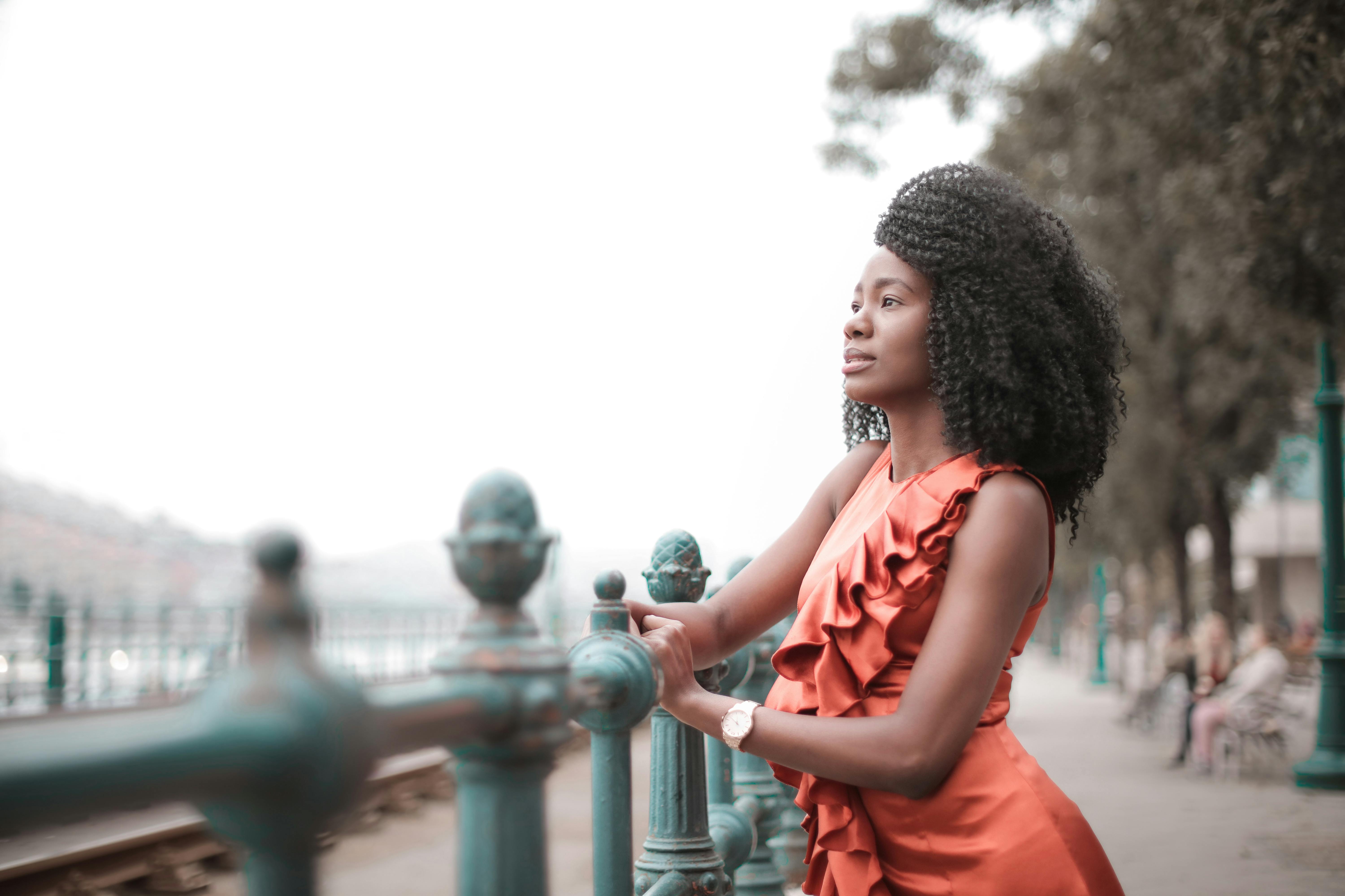 一位穿着橙色连衣裙的优雅女子站在栏杆旁