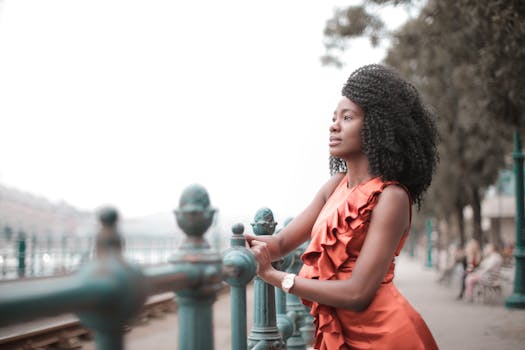 一位穿着橙色连衣裙的优雅女子站在栏杆旁