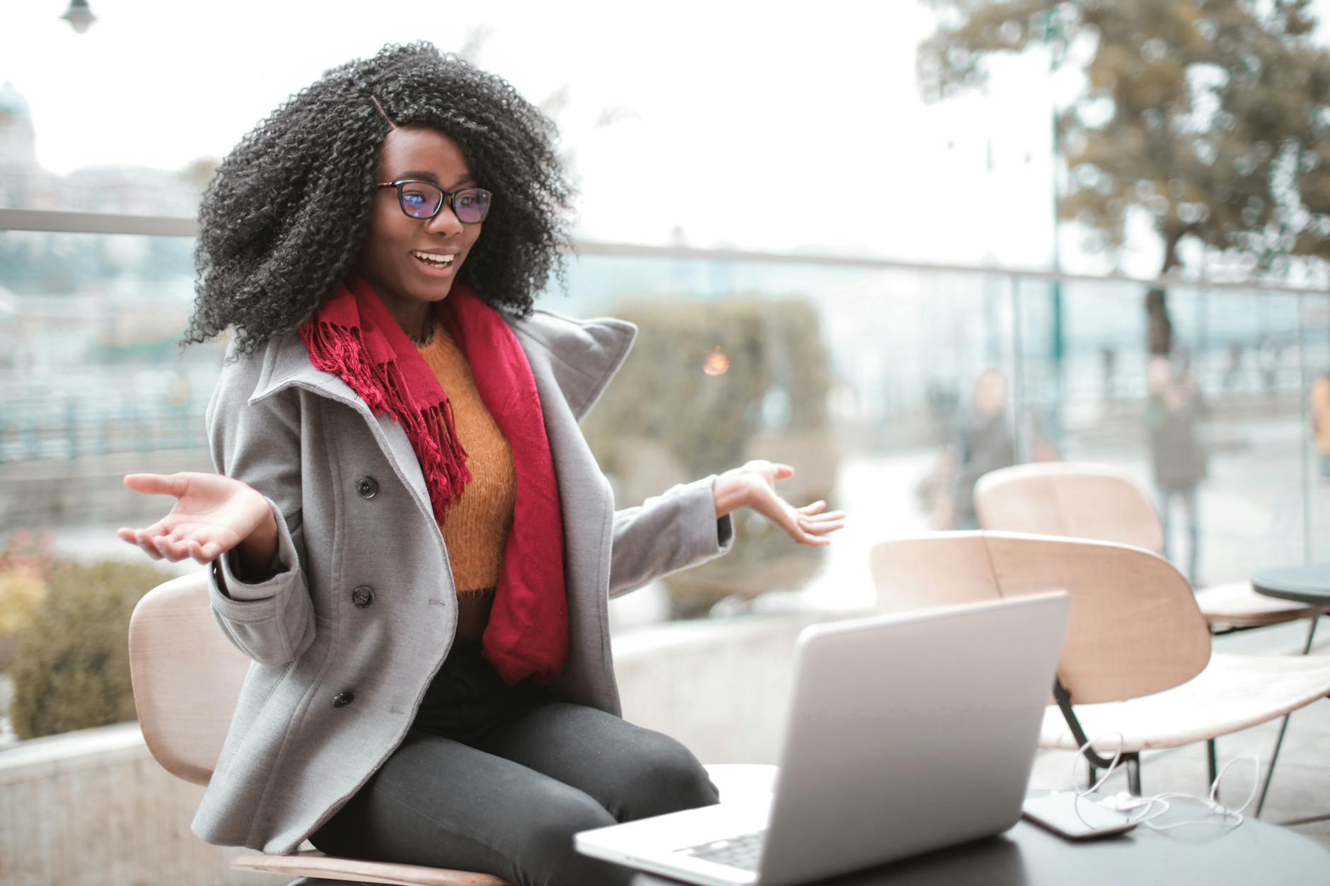 즐겁게 흥분한 아프리카계 미국인 여성은 노트북으로 화상 통화를 하고 현대적인 카페에 앉아 웃고 몸짓을 합니다.