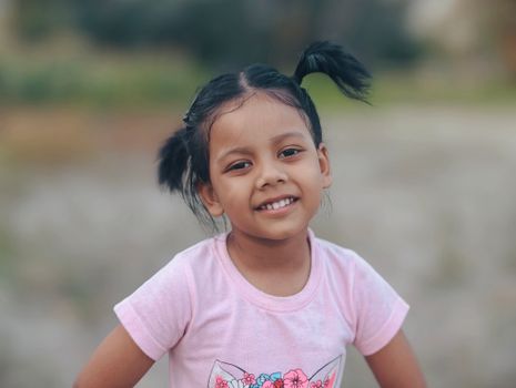 A cheerful young girl with pigtails smiles at the camera while standing outdoors.