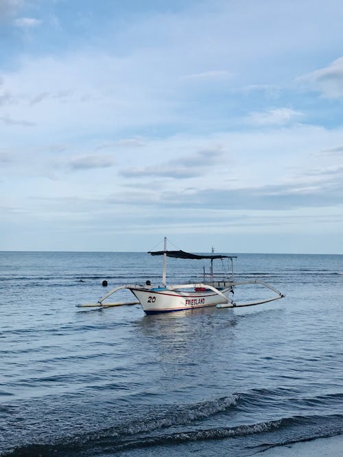 Traditional fishing boat with canopy floating on calm water of sea against cloudy blue sky