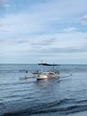平静的海面上，一叶带伞篷的传统渔船漂浮着，映衬着多云的蓝天