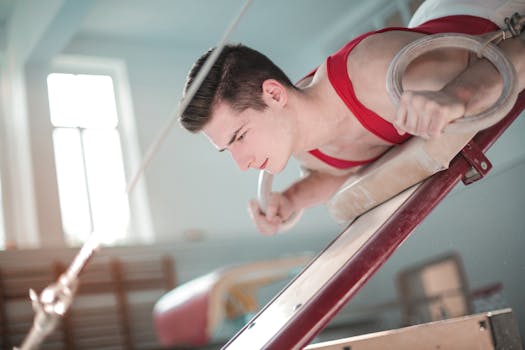 Focused male gymnast in red attire practicing on gymnastic rings indoors, showcasing strength and balance.