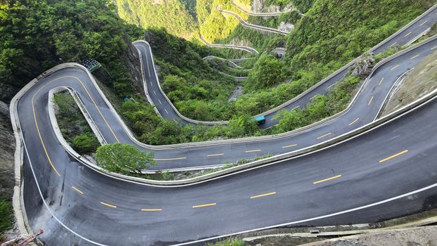 A breathtaking aerial view of a winding road through lush green mountains.