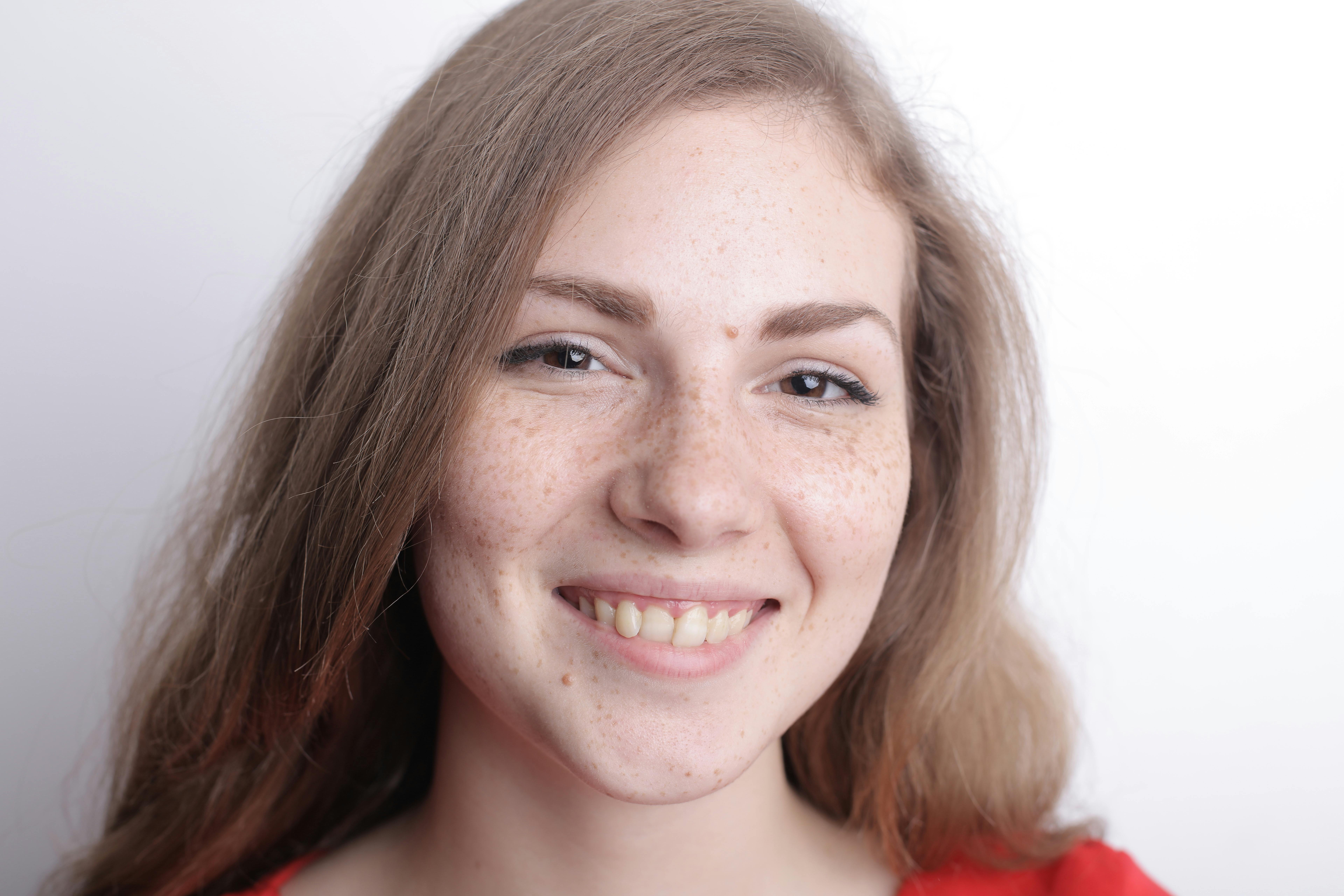 这幅特写肖像画得很快乐，描绘了一位面带微笑、有雀斑的女人，背景是白色的