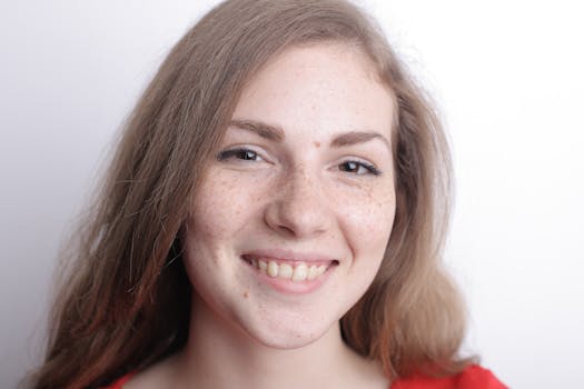 这幅特写肖像画得很快乐，描绘了一位面带微笑、有雀斑的女人，背景是白色的