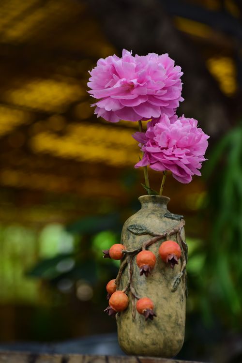 Free Bright pink peonies in a rustic vase with ornaments, showcasing a natural and artistic display. Stock Photo