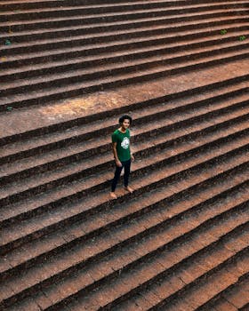 A young man in a green shirt stands on a wide, outdoor staircase, viewed from above.