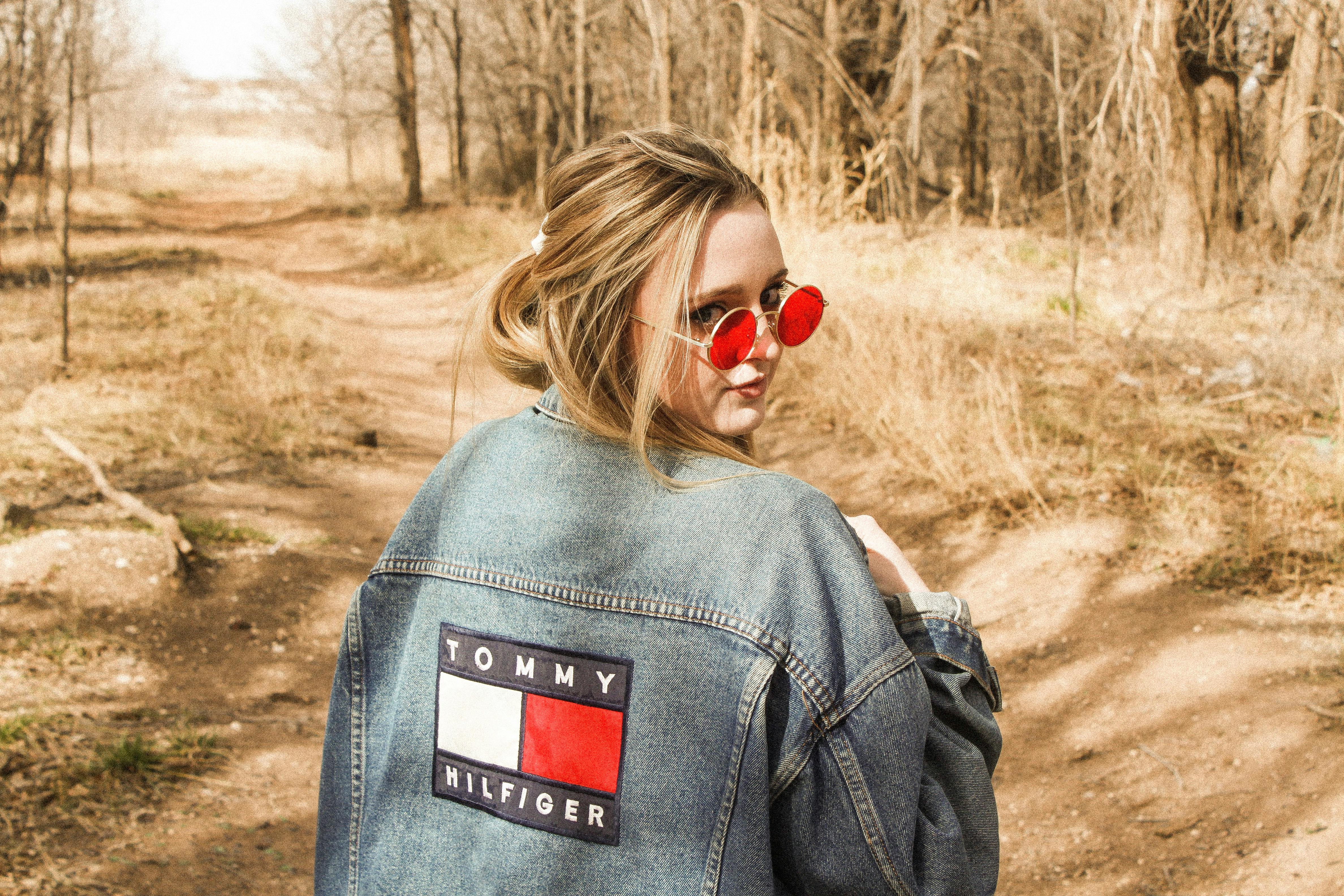 一位戴着太阳镜、身穿牛仔夹克的时尚女子走过林间小路