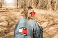 戴着太阳镜和牛仔夹克的时尚女人走过树木繁茂的小路