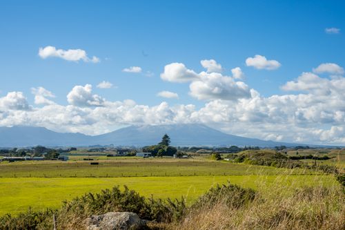 Free A picturesque landscape featuring Mount Taranaki with vast green fields under a bright blue sky. Stock Photo