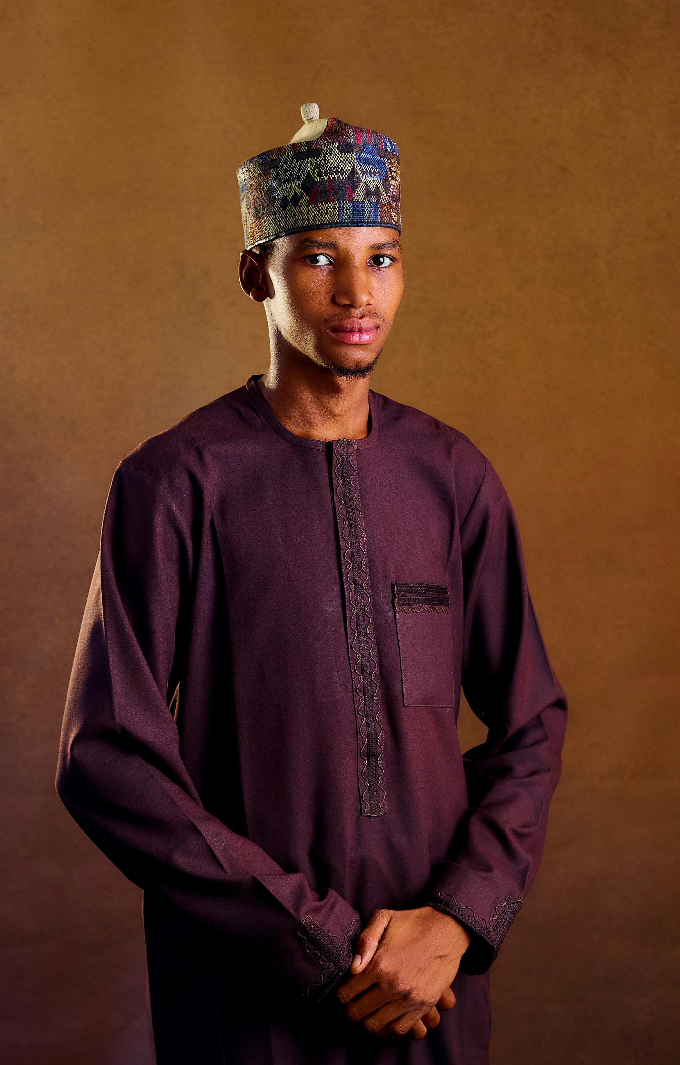 Portrait of a man in traditional African attire with a colorful hat and embroidered robe.