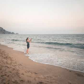 A woman captures the serene beauty of Alanya beach at sunset, Türkiye.