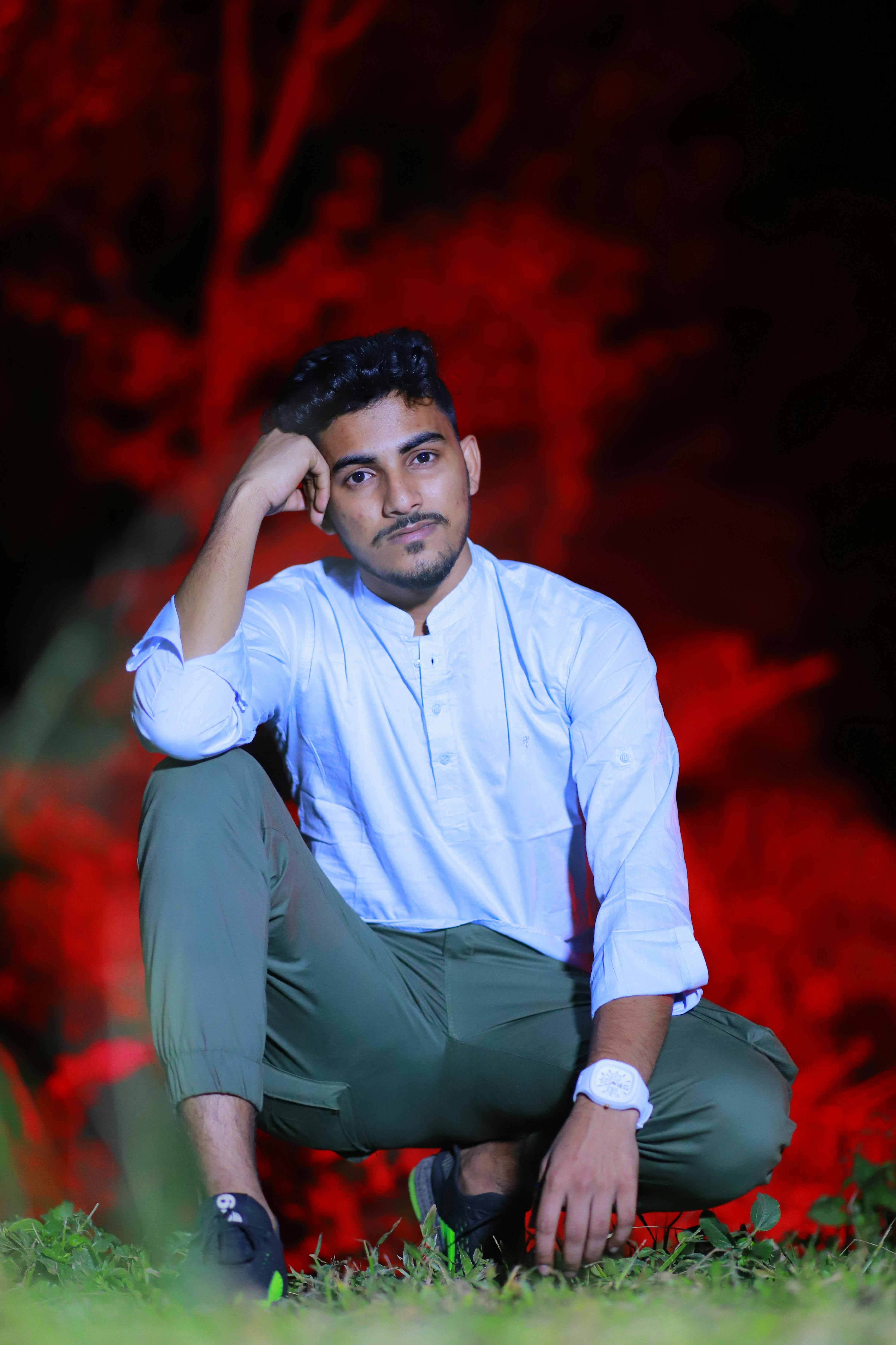 A seated man in casual attire poses thoughtfully in an outdoor setting.