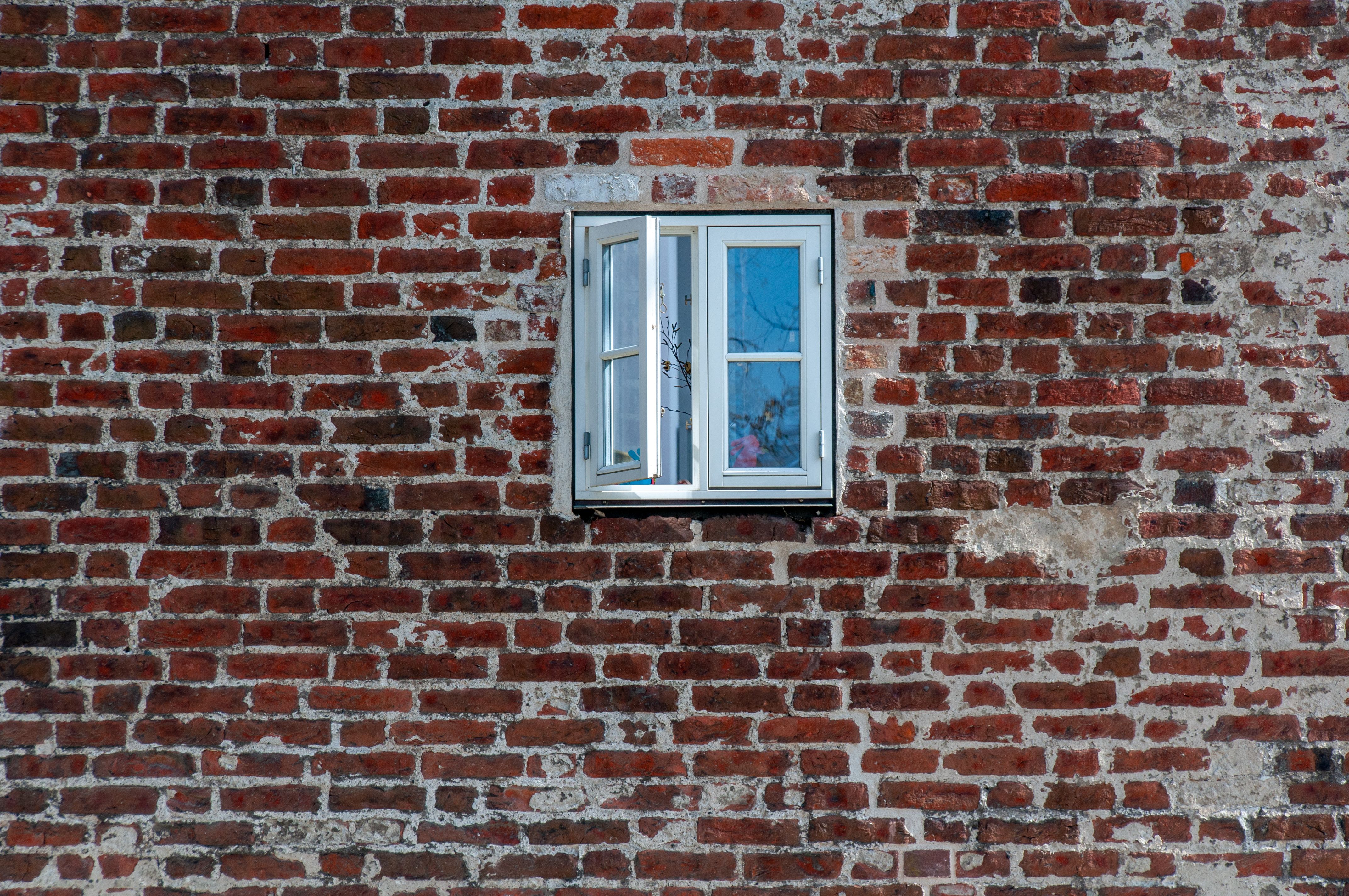 Geöffnetes weißes Fenster in einer alten roten Backsteinwand, Symbol für Lüftung und Feuchtigkeit im Altbau.