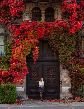 A woman stands by a historic door adorned with vibrant autumn ivy, showcasing seasonal beauty.