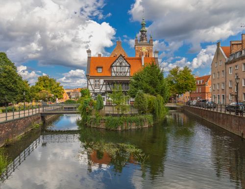 Free Picturesque scene of Gdańsk's historic architecture along a serene canal under a vibrant sky. Stock Photo