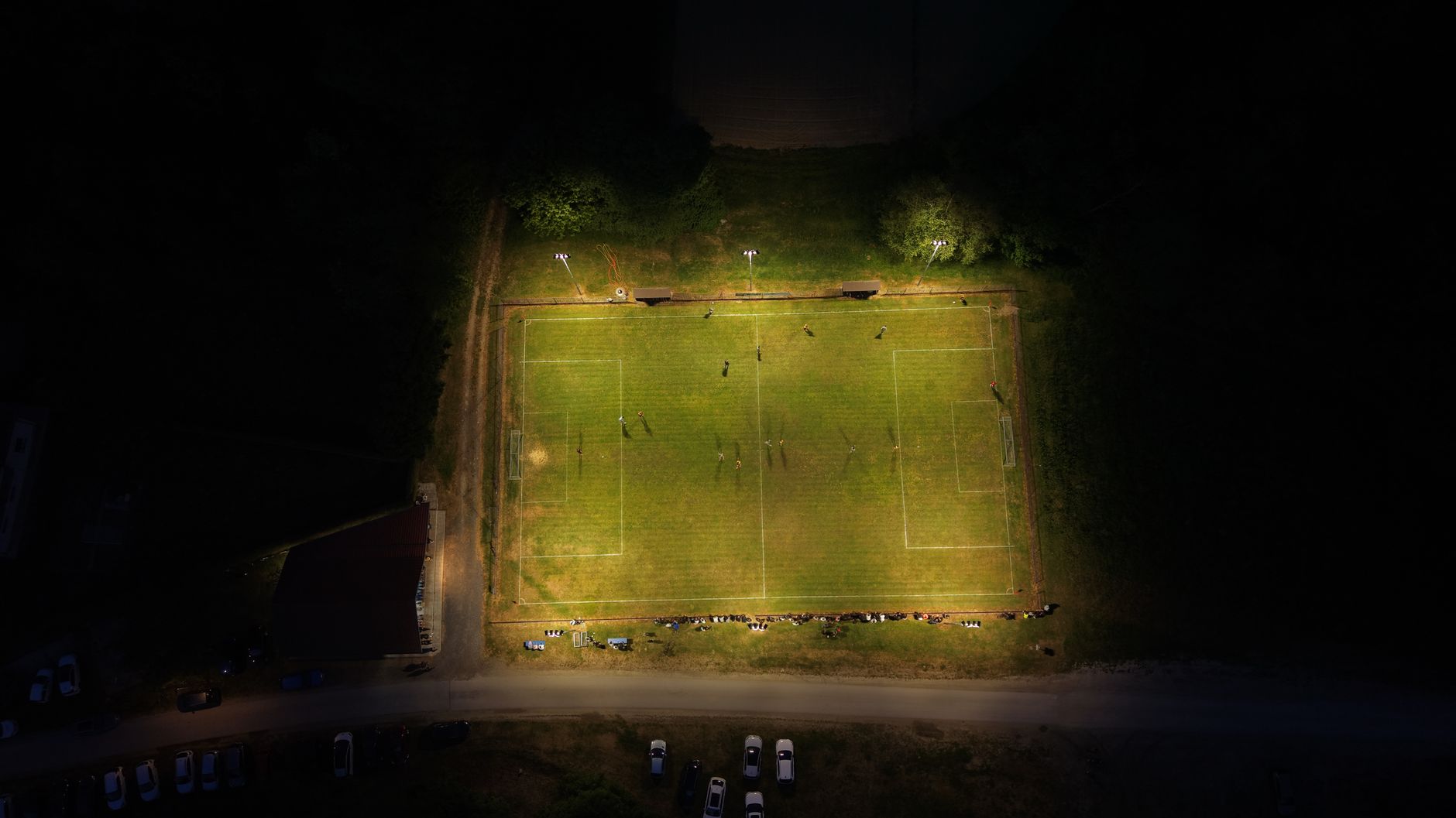 Aerial shot of a lit soccer field at night, with players and spectators visible.