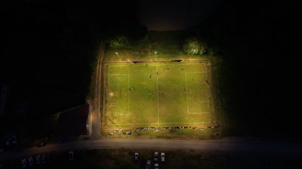 Aerial shot of a lit soccer field at night, with players and spectators visible.