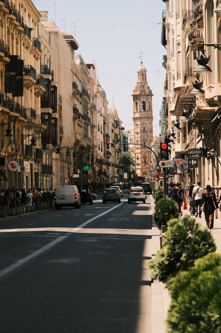Bustling street in Valencia with historic bell tower and vibrant city life.