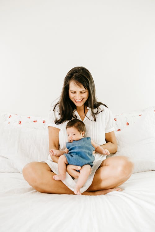 침대에 앉아있는 동안 그녀의 아기를 들고 웃는 여자의 사진