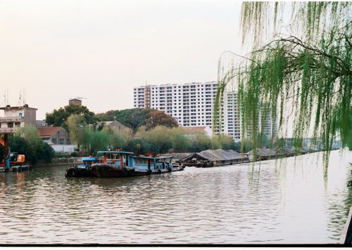 Free A tranquil river with boats, urban buildings, and lush greenery. Stock Photo