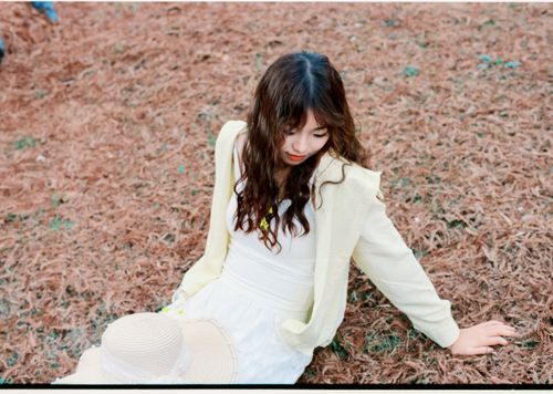 Free Woman sitting on dried leaves outdoors, wearing white outfit and yellow jacket, relaxing. Stock Photo