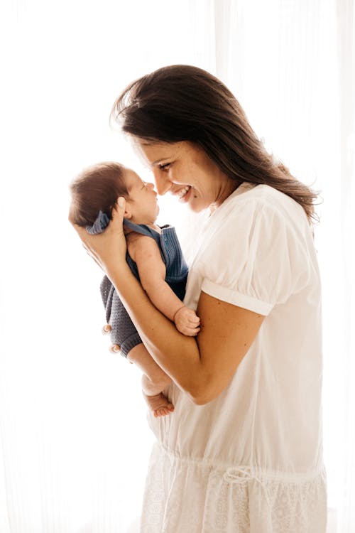 Free Side View Photo of Smiling Woman Carrying Her Baby Stock Photo