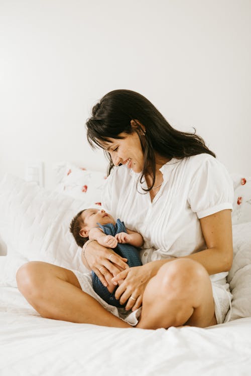 Photo D'une Femme Souriante Portant Son Bébé Assis Sur Un Lit