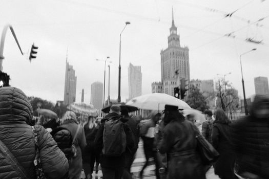 Monochrome city street scene with busy pedestrian crowd and urban skyline backdrop.
