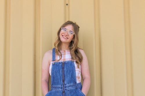 Photo De Femme Souriante En Salopette En Denim Bleu Et Lunettes Encadrées Marron Posant