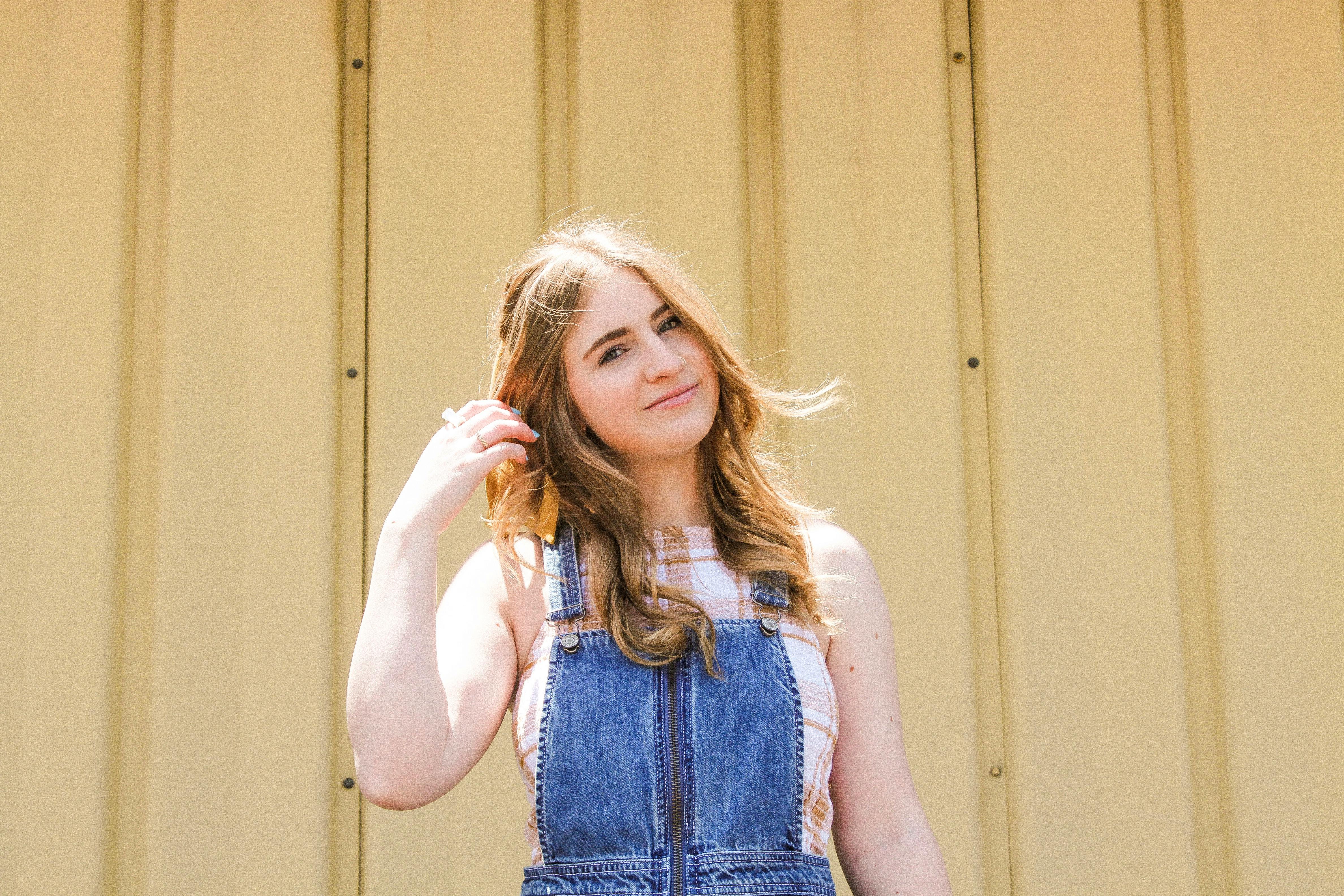 一名年轻女子穿着牛仔裤，在黄色背景下随意摆着姿势，笑容温暖