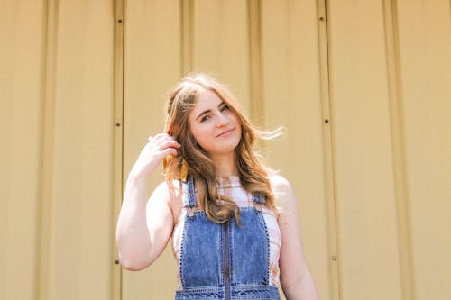 Free Photo of Smiling Woman in Blue Denim Dungaree Standing Beside Brown Wall Stock Photo