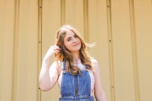 一名年轻女子穿着牛仔裤，在黄色背景下随意摆着姿势，笑容温暖