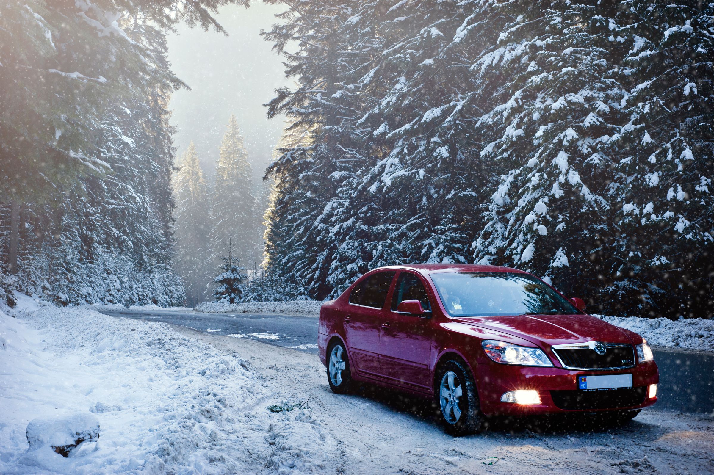 Car driving on a plowed snowy forest road during winter snowfall