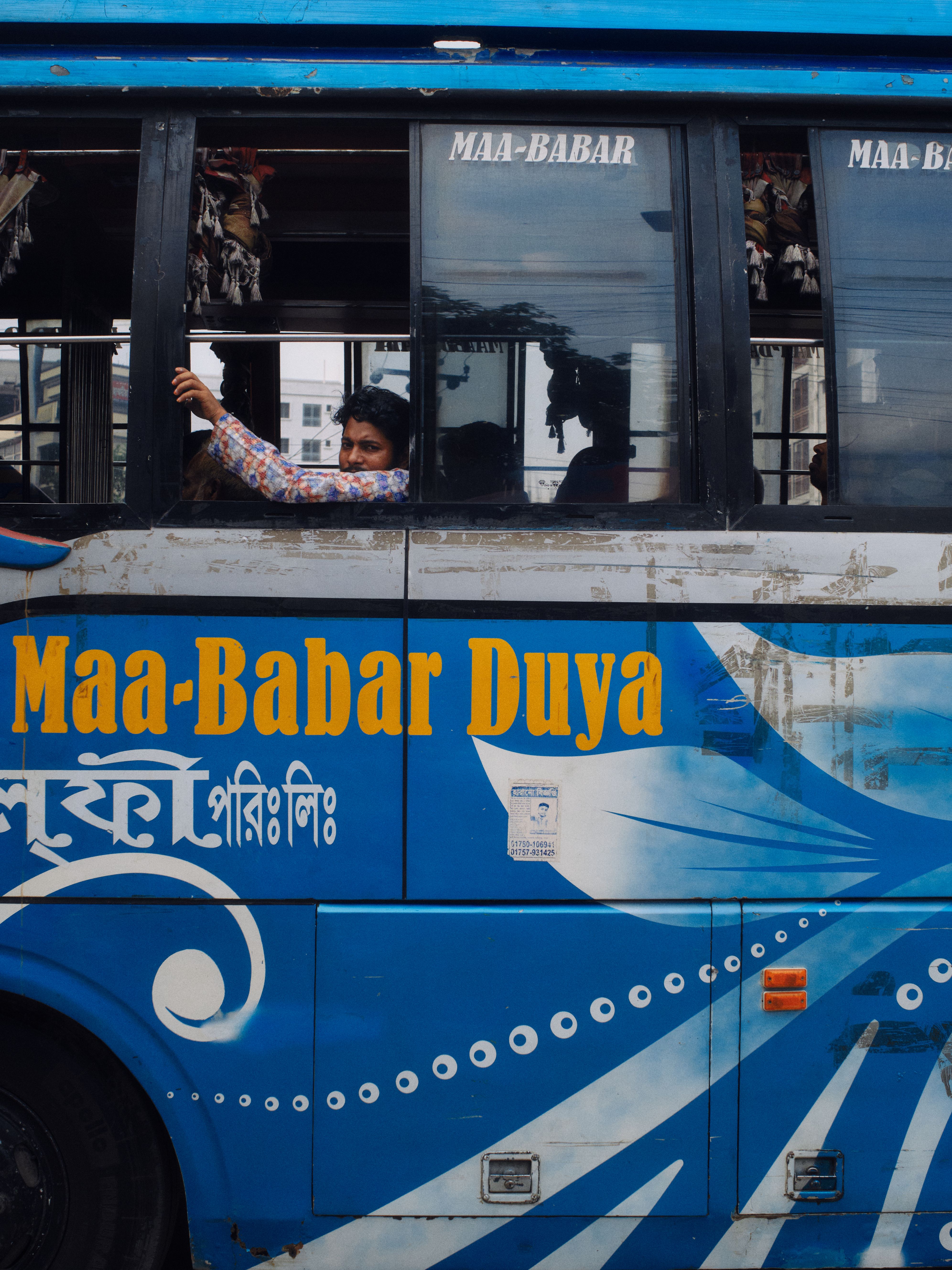 A vibrant blue public transportation bus with passengers in Dhaka, Bangladesh.