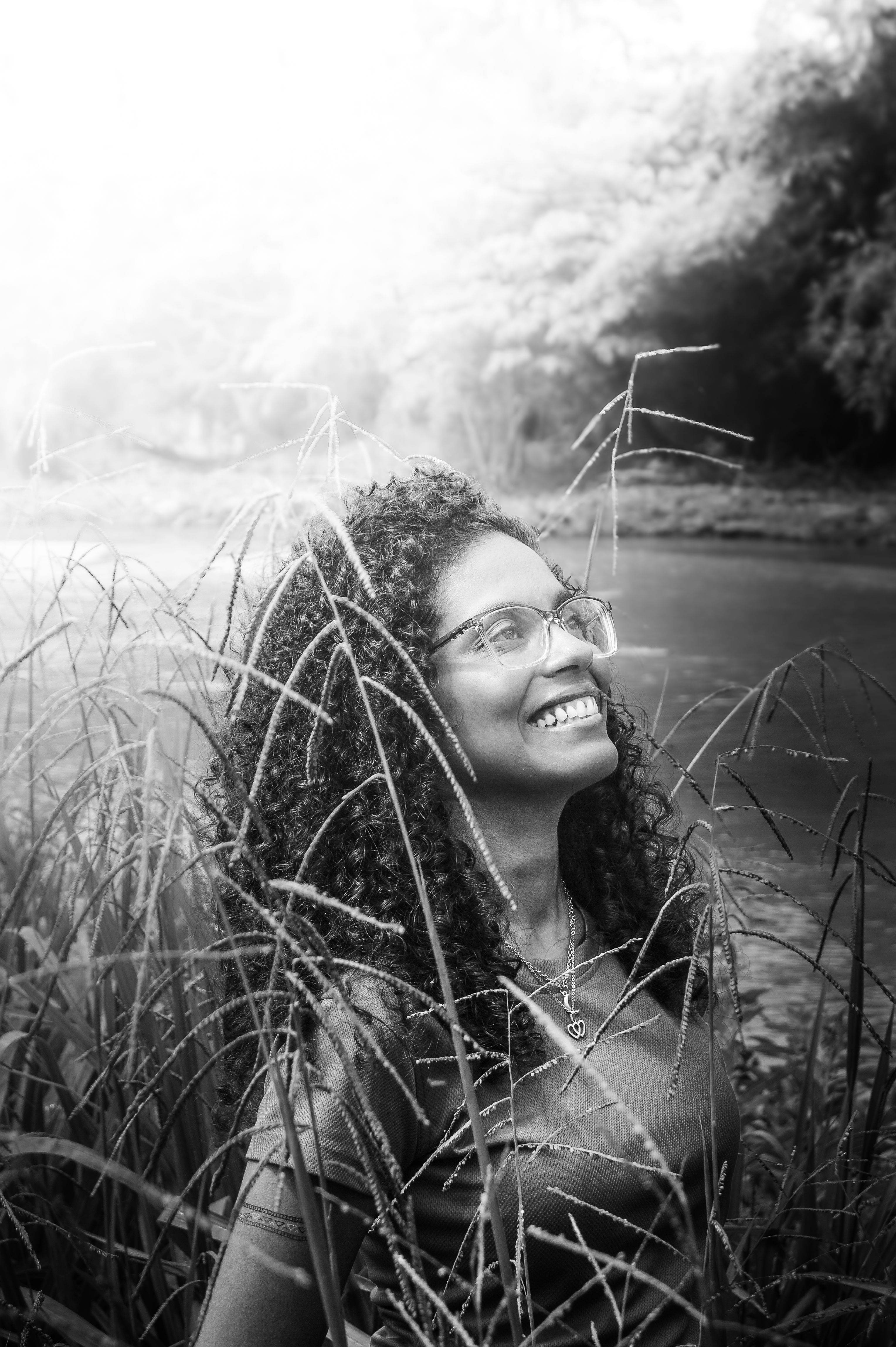 Charming black and white portrait of a woman smiling amidst nature, with a bright and joyful expression.