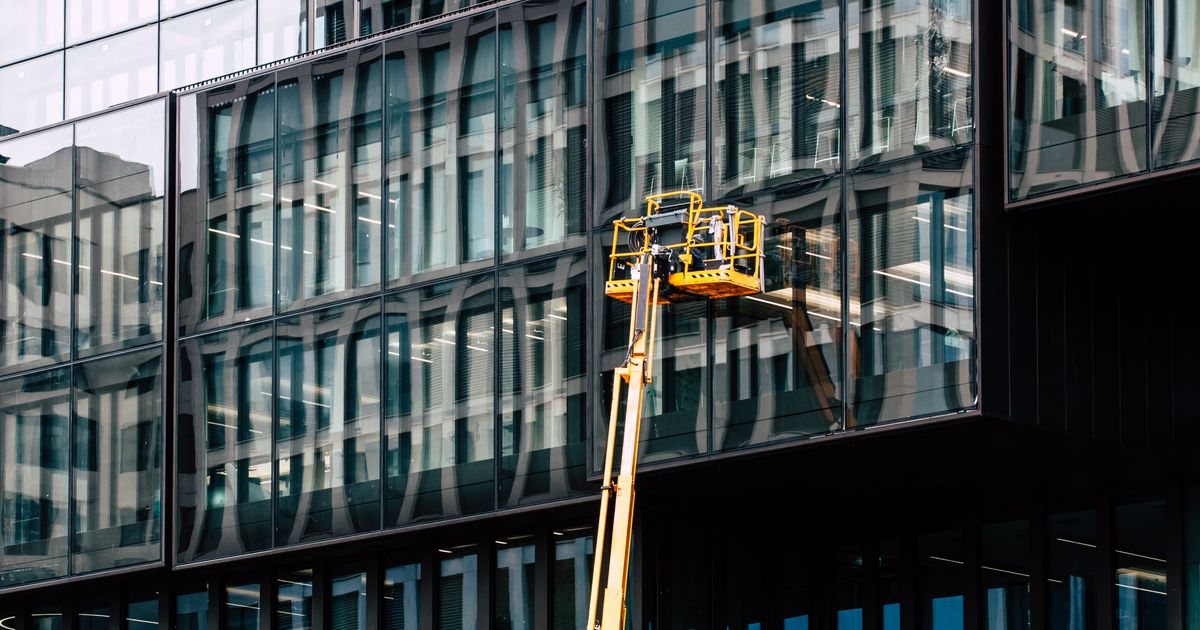 Facharbeiter reinigen auf einer Hebebühne die Glasfassade eines modernen Bürogebäudes