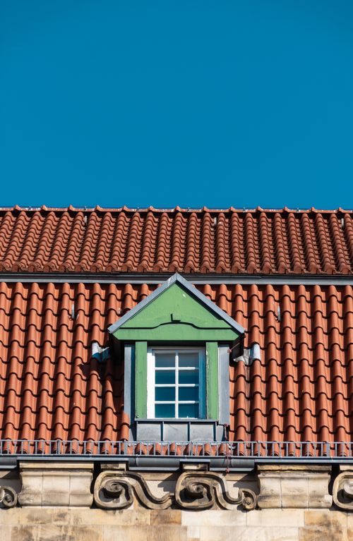 Free Close-up view of a classic red-tiled roof with decorative window and ornate moldings under a clear blue sky. Stock Photo