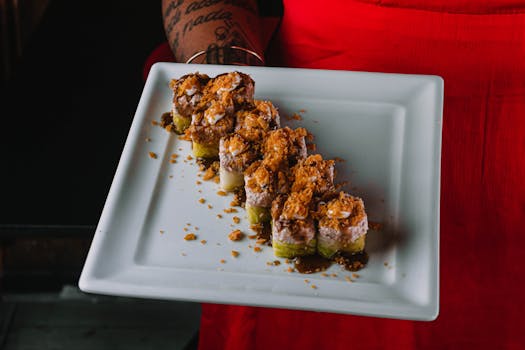 A vibrant sushi roll topped with crispy flakes, beautifully presented on a white square plate.