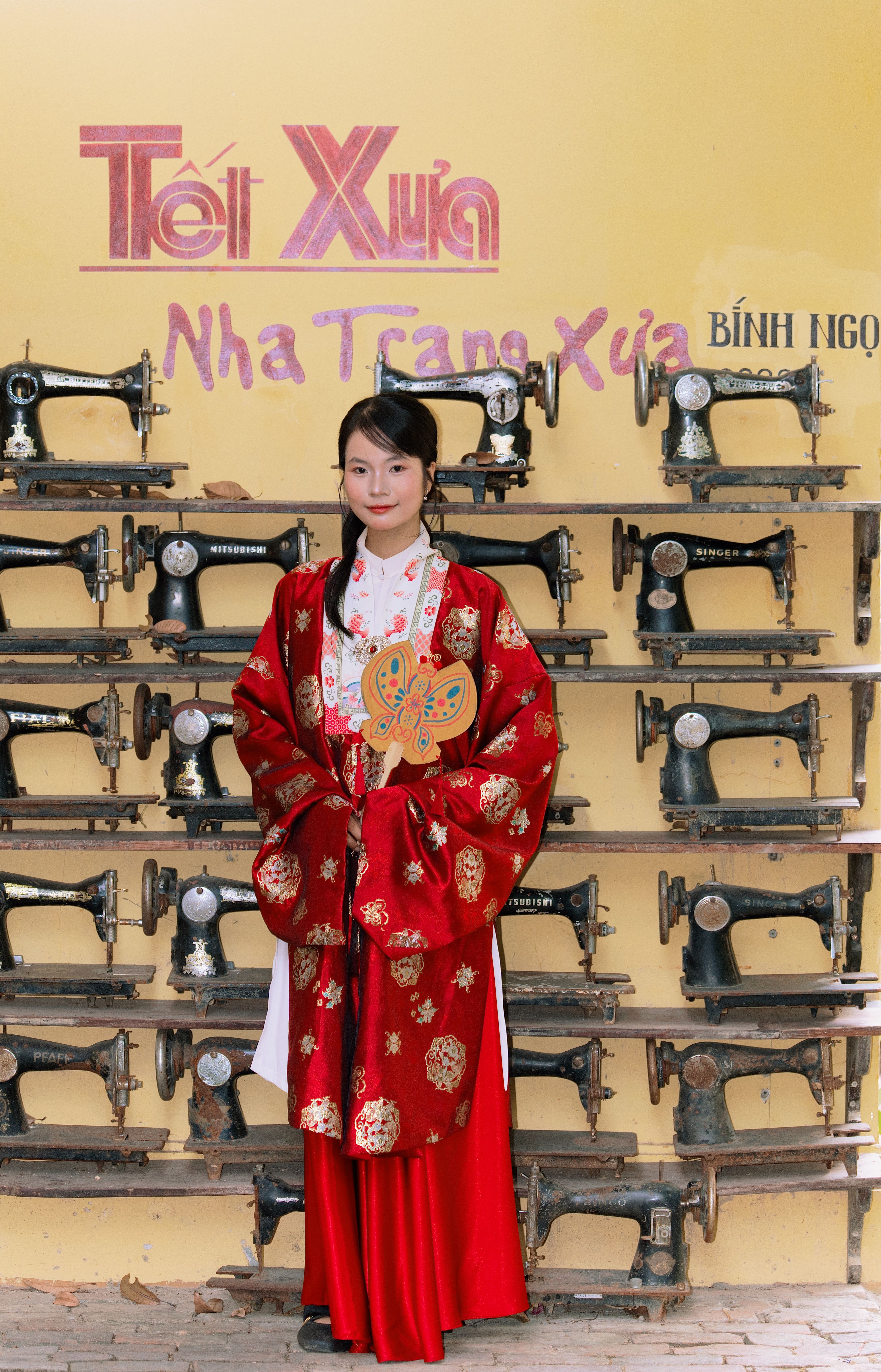 Woman in traditional attire beside vintage sewing machines in Vietnam.