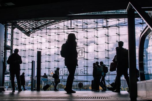 Silhouetted travelers inside a contemporary glass building with a vibrant sky backdrop.