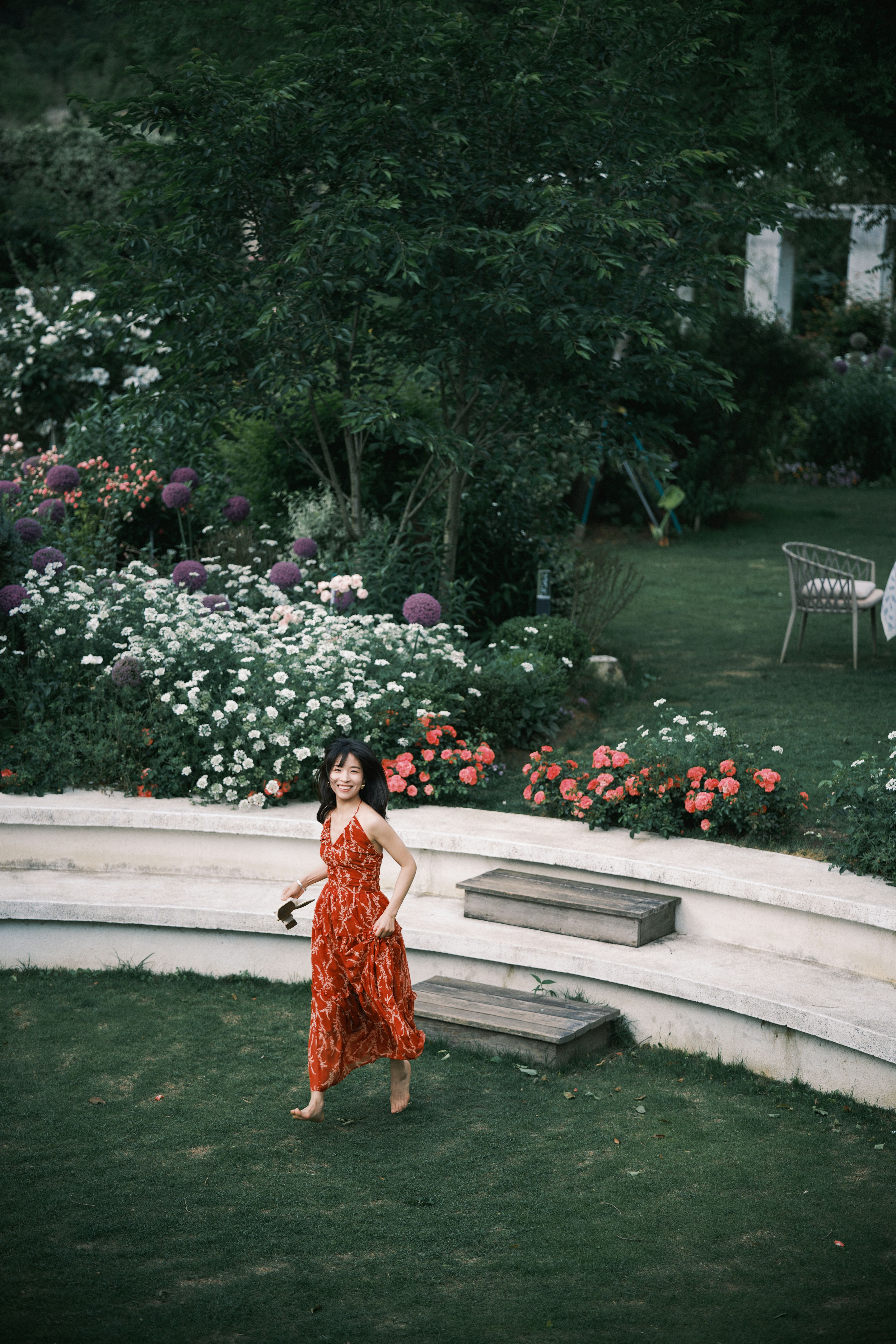 A woman in a red dress walks in a lush garden filled with colorful flowers.