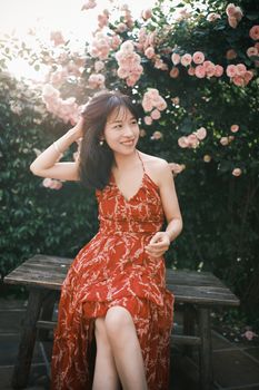 Smiling young woman in a floral dress enjoying a sunny day in a rose garden.