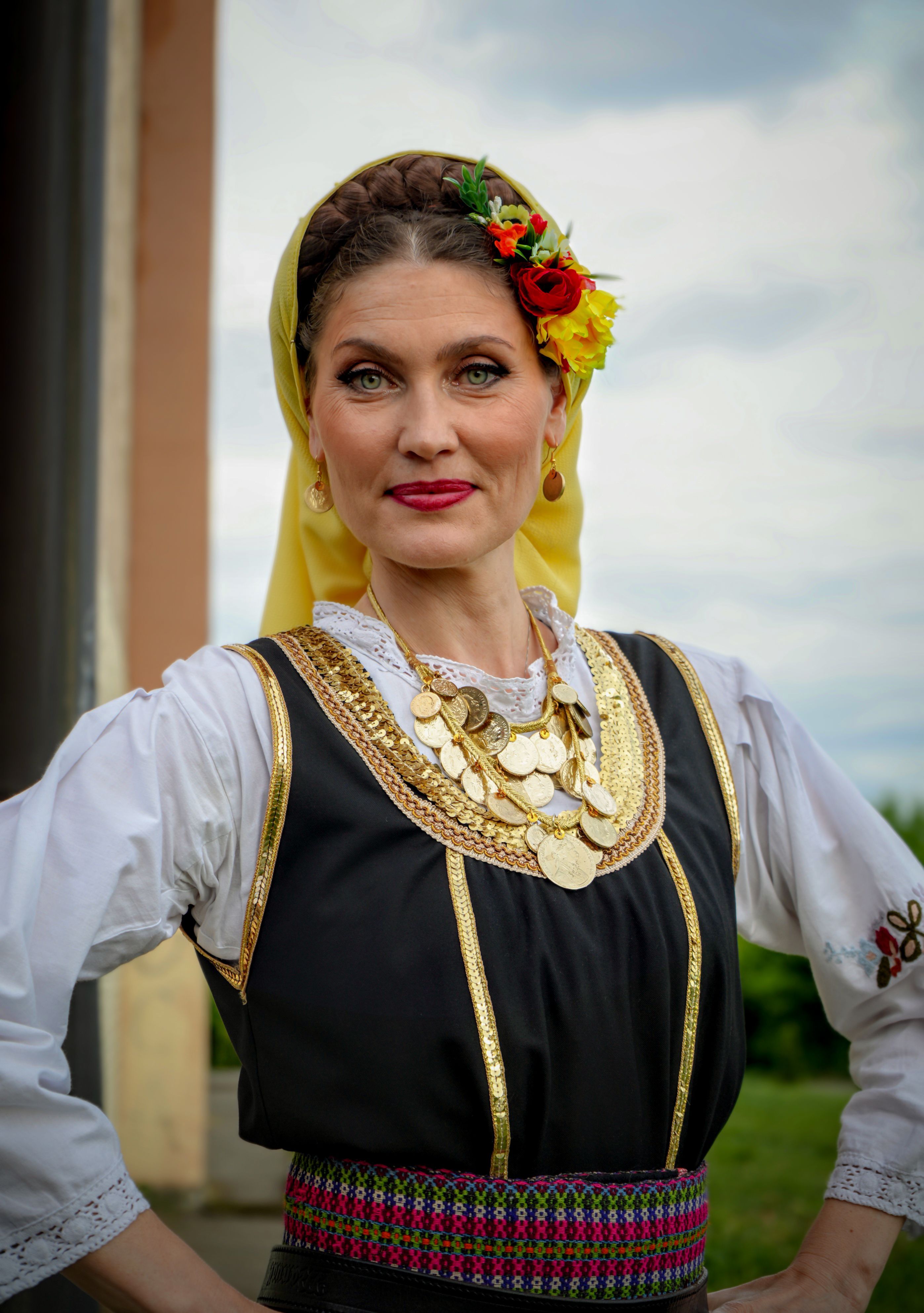 Woman wearing traditional Balkan attire with floral headpiece, posing confidently.