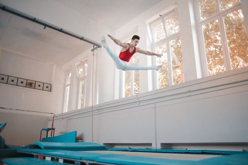 Free Young sportsman in sportswear doing split in air while jumping on trampoline in gym Stock Photo