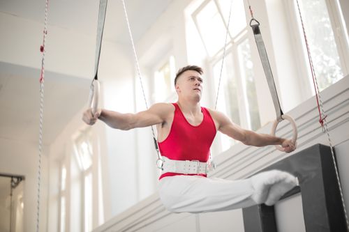 Free Adult male gymnast demonstrating strength on gym rings indoors. Stock Photo