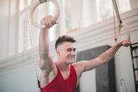 男体操运动员在室内环上微笑锻炼，展现健康与快乐